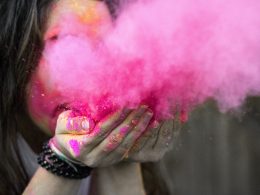 Woman blowing a cloud of pink Holi powder from her hands